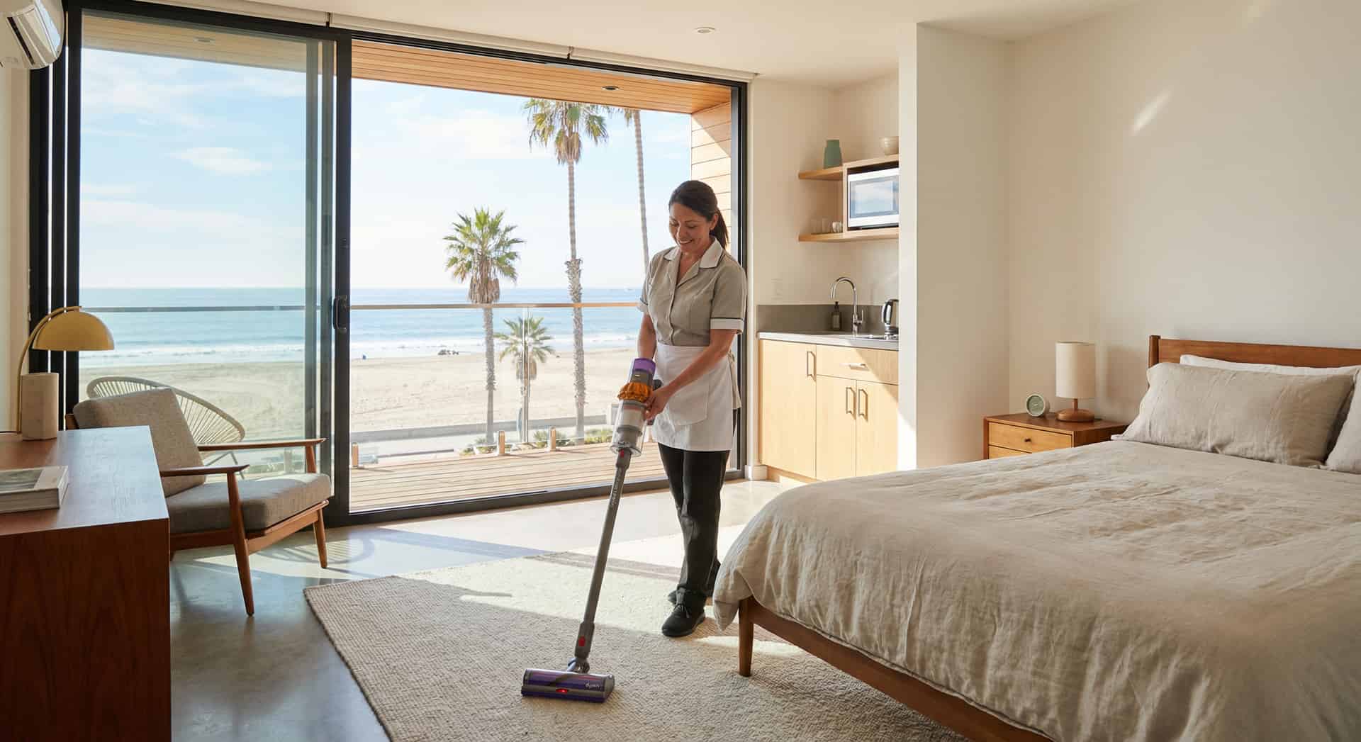 Professional cleaner vacuuming a bright studio apartment overlooking the beach
